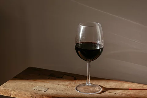 A glass of red wine sits on a wooden bench.