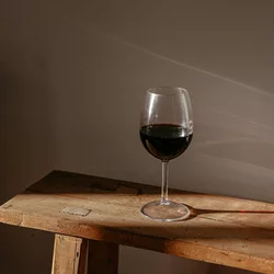 A glass of red wine sits on a wooden bench.